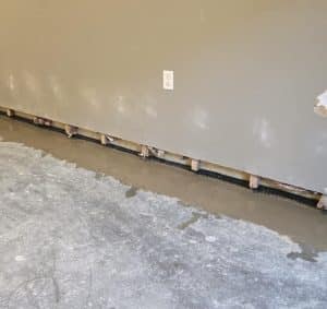 A partially repaired wall with missing lower drywall reveals wooden studs and insulation. Fresh concrete is visible along the base, conveying ongoing construction.