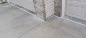 Concrete driveway and garage with sealed edges, featuring beige brick and siding. The scene is orderly and well-maintained, conveying neatness.